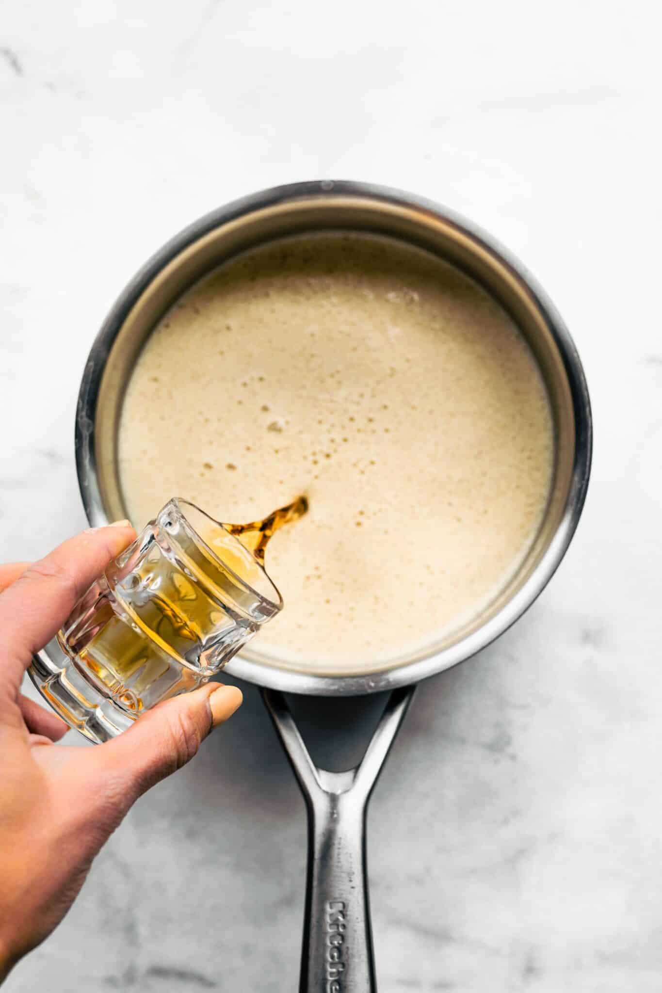 A woman's hands pouring rum into a pot of homemade egg nog.