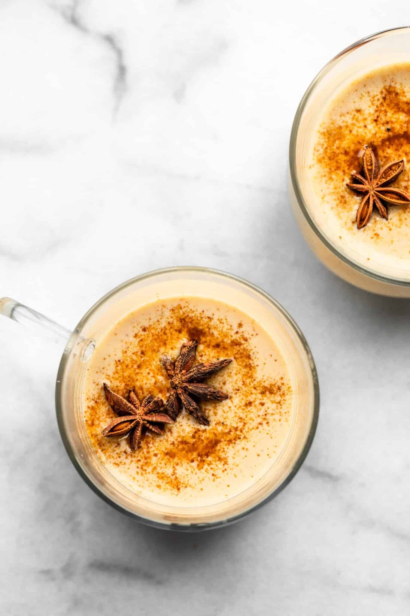Overhead photo of two glass mugs of dairy free eggnog topped with star anise.