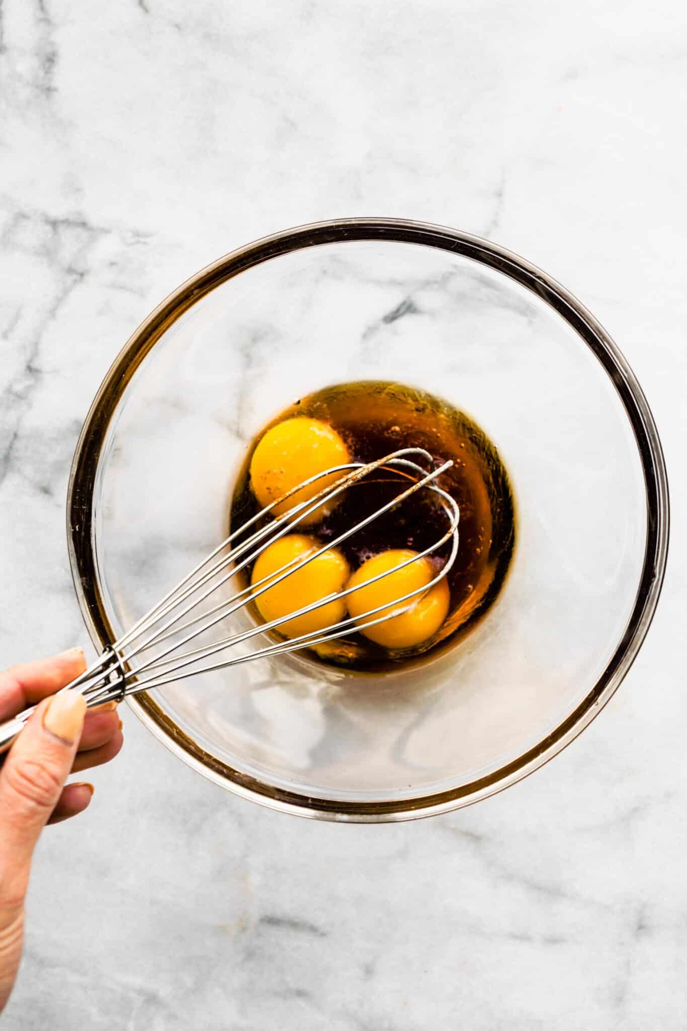 Whisking together egg yolks and maple syrup in a glass mixing bowl.