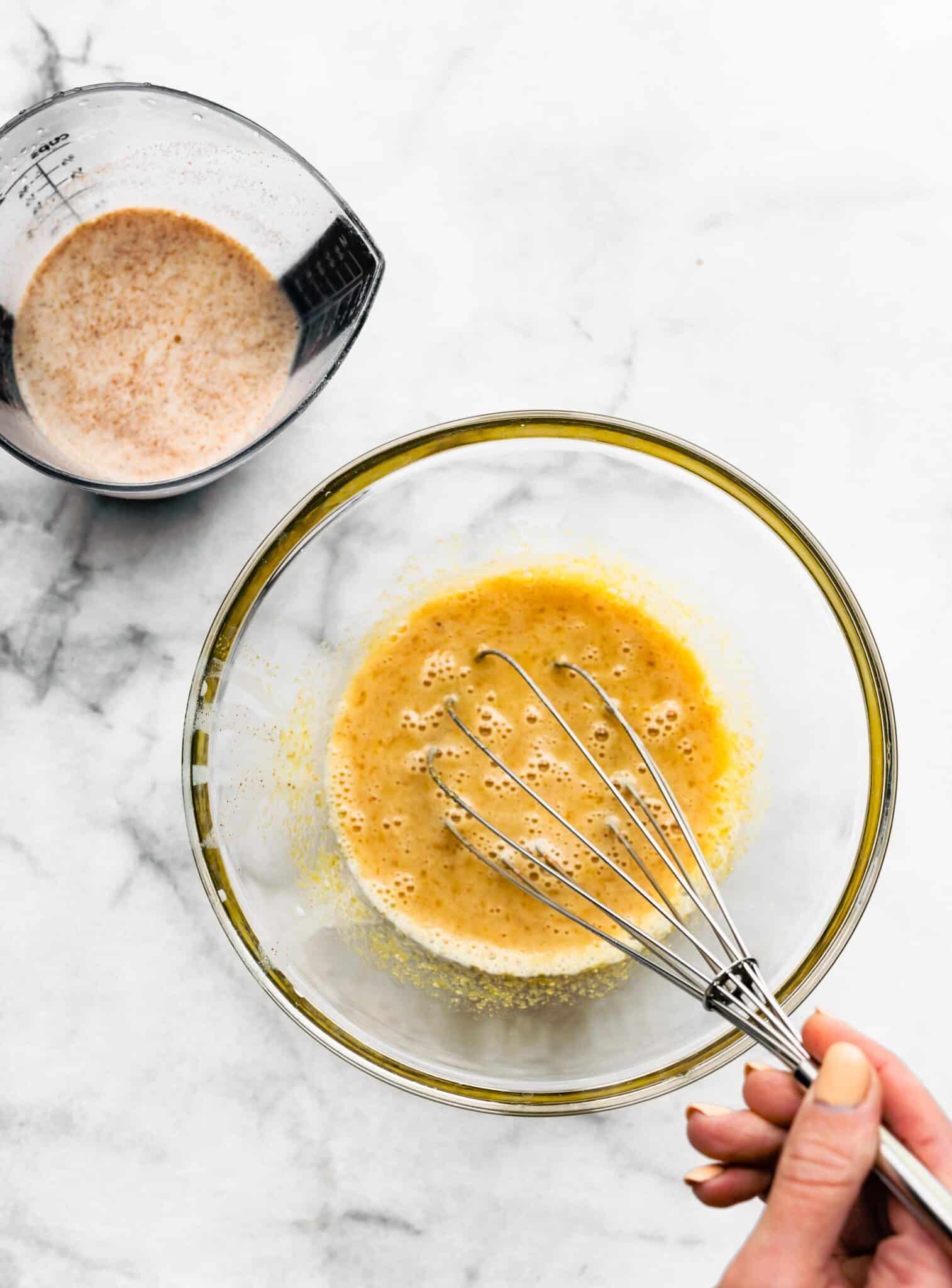 Whisking the milk mixture into the egg yolk mixture for eggnog.