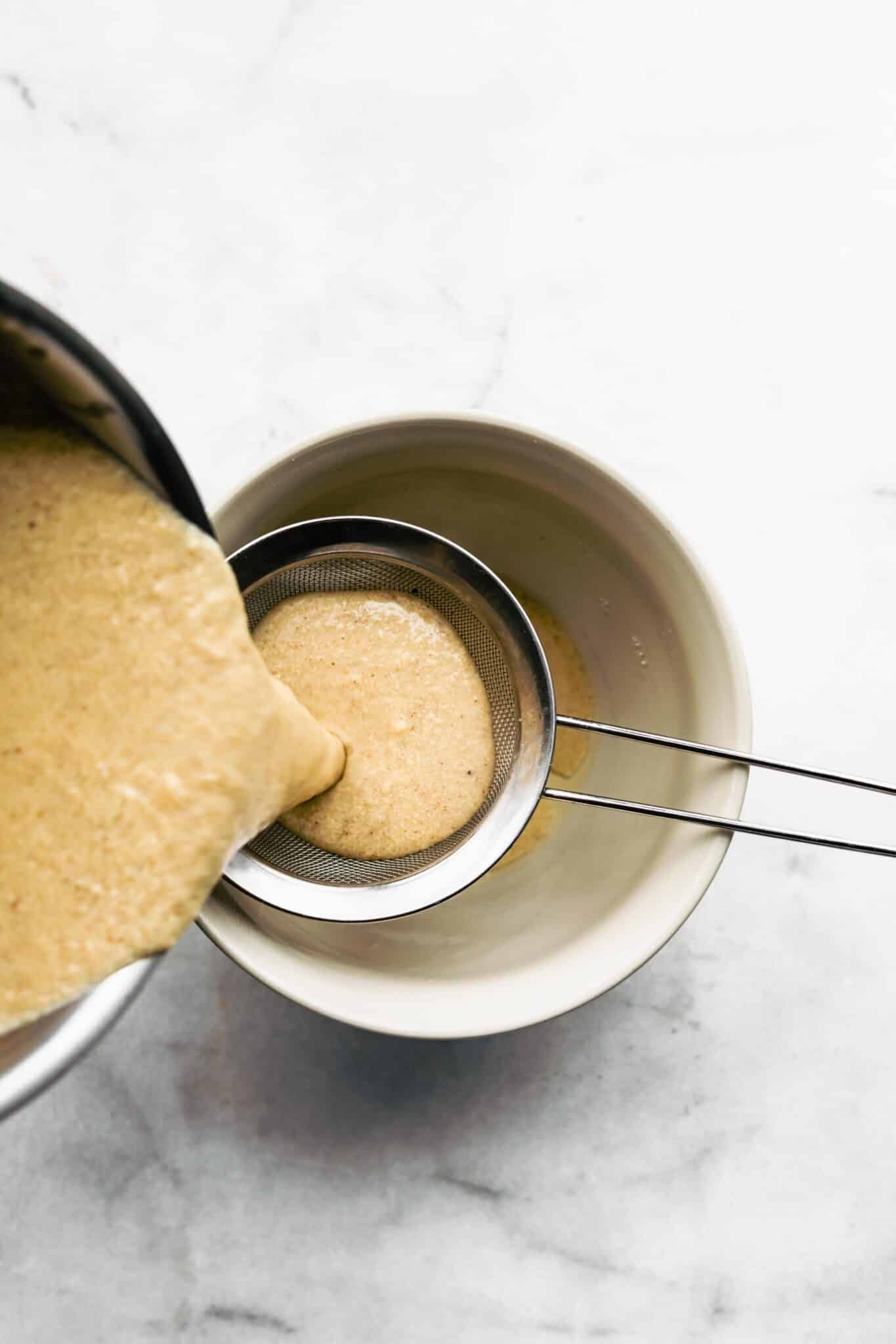 Pouring dairy free egg nog through a strainer over a bowl.