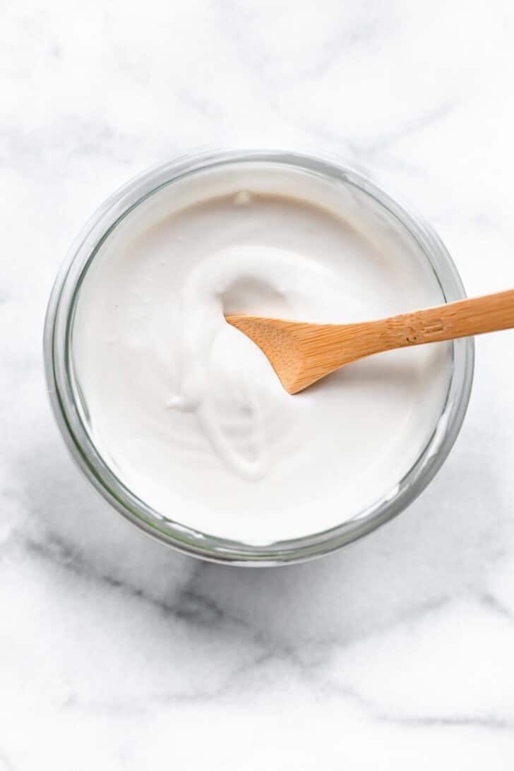 A wooden spoon in a jar of vegan coconut yogurt.