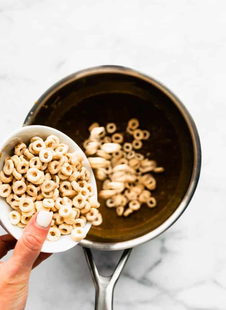 A woman's hand pouring gluten free puffed cereal into a saucepan.