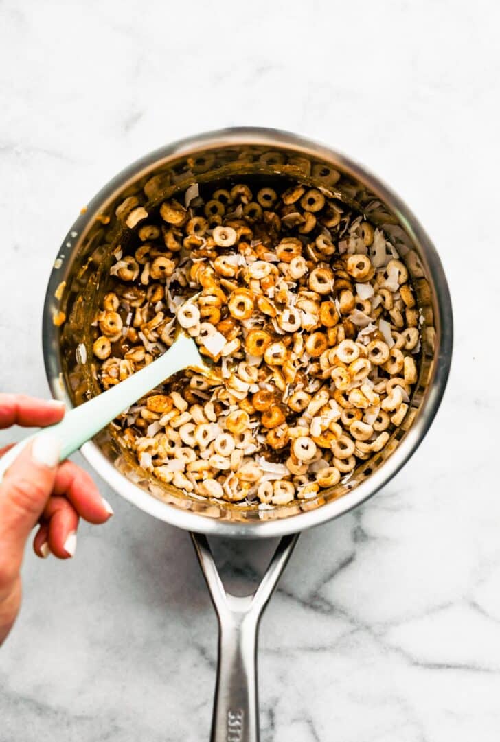 Stirring gluten free cereal into a honey mixture with a white spatula.
