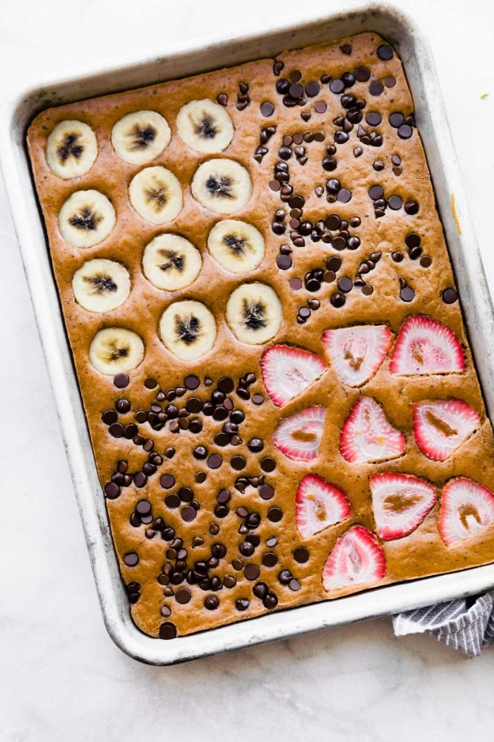 sheet pan keto pancakes with toppings of sliced bananas, strawberries, and chocolate chips