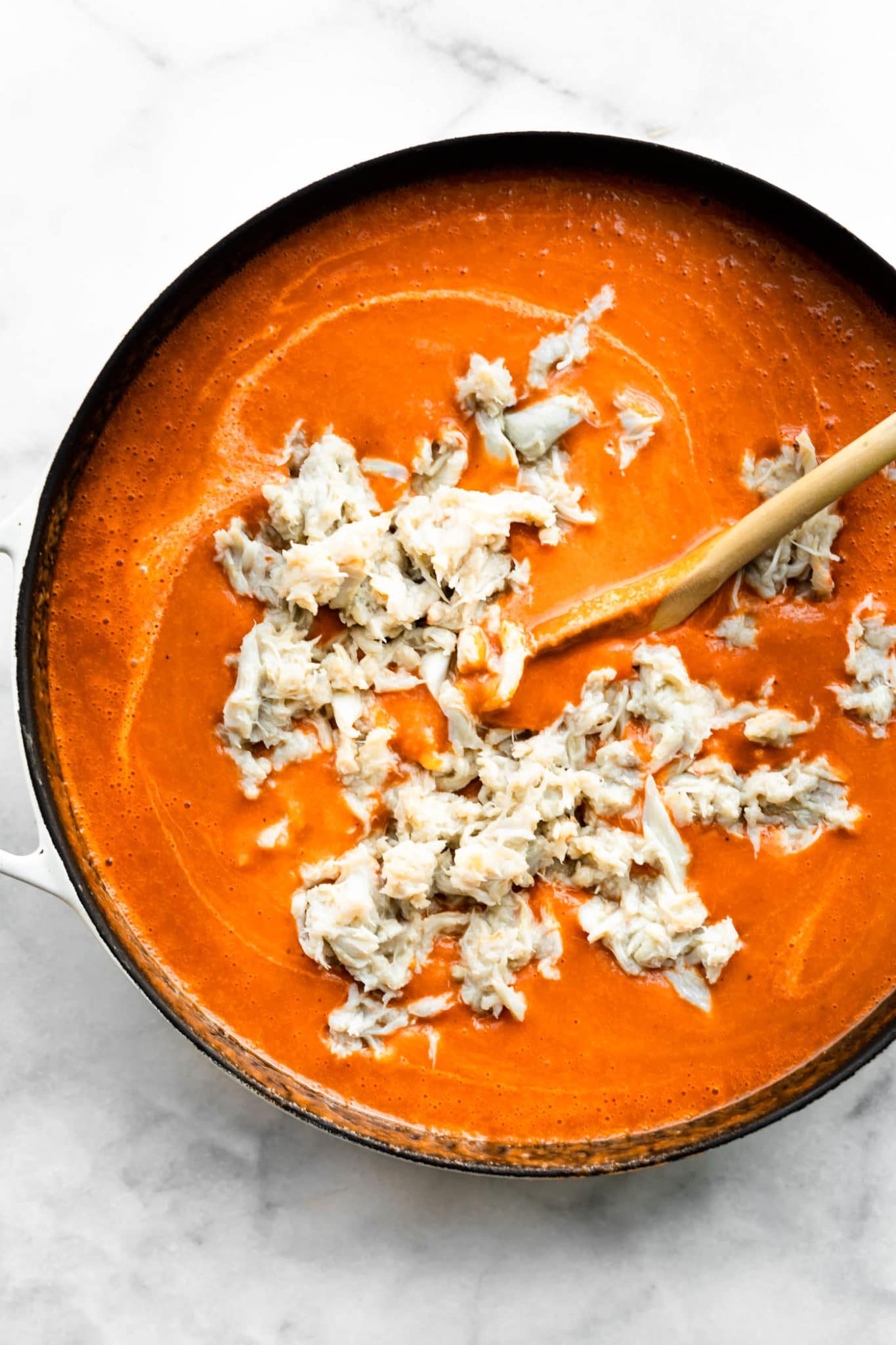 crab meat being swirled into tomato crab bisque with a wooden spoon