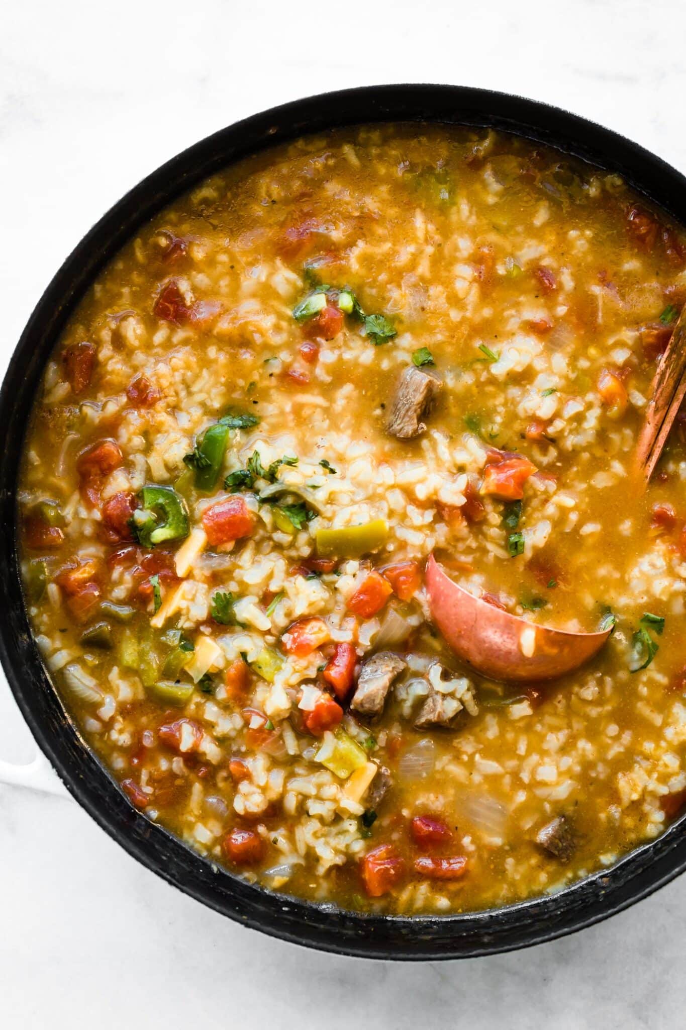 Up close overhead photo of fajita steak soup in a pot with a copper ladle.
