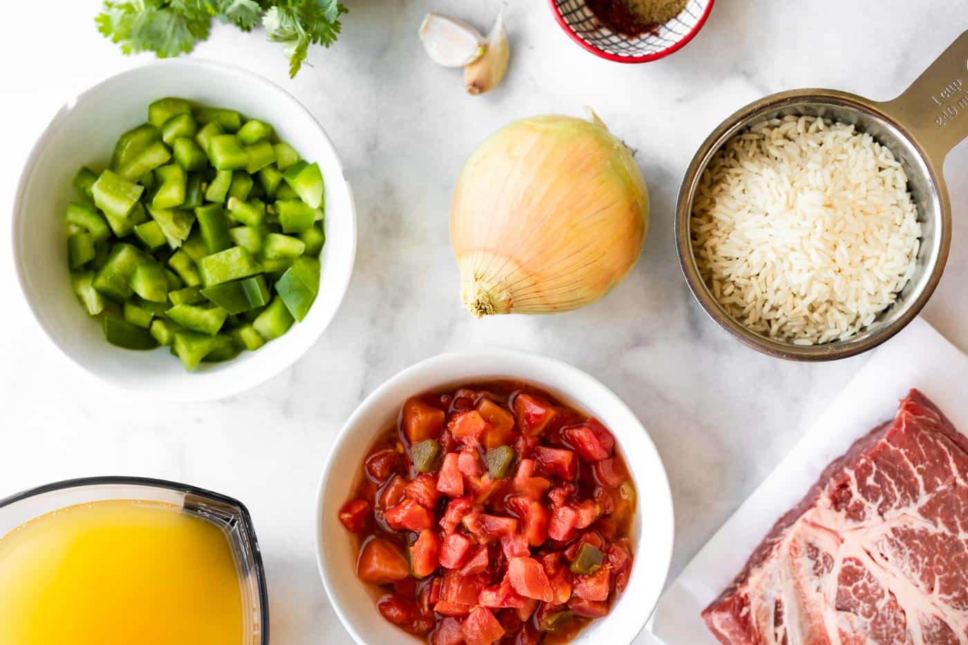 Bowls of ingredients like diced tomatoes with green chiles and rice on a marble countertop.