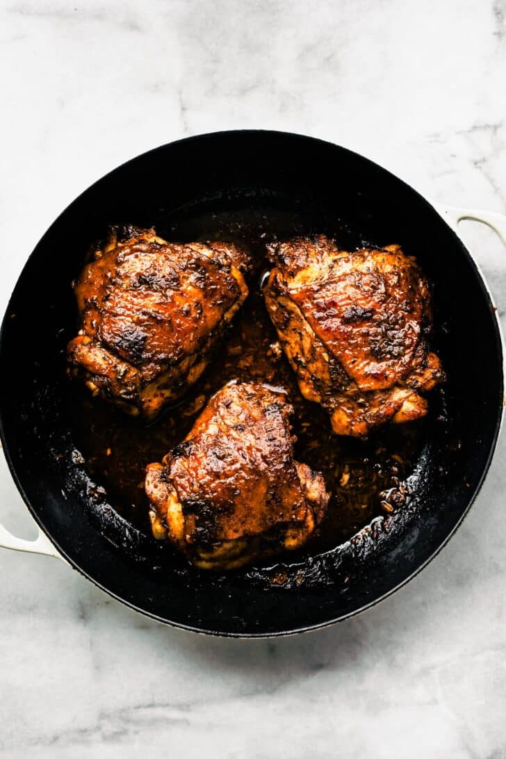 Cooked jerk chicken thighs in a cast-iron skillet, skin crisped and sauce pooled at the bottom.