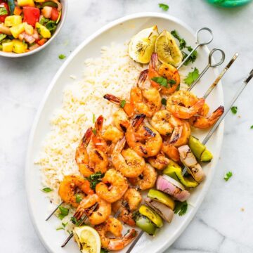 Overhead image of grilled skewered shrimp on a platter of rice with a side of watermelon salsa.