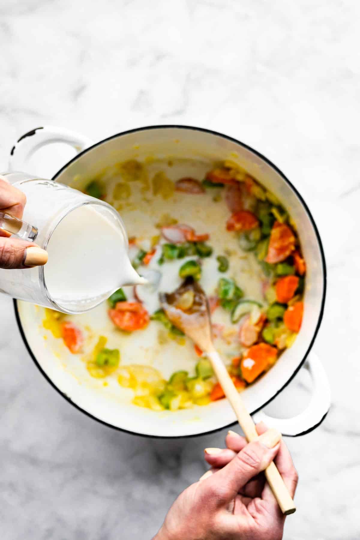Coconut milk poured into a pot of sauteed carrots, celery and onion.