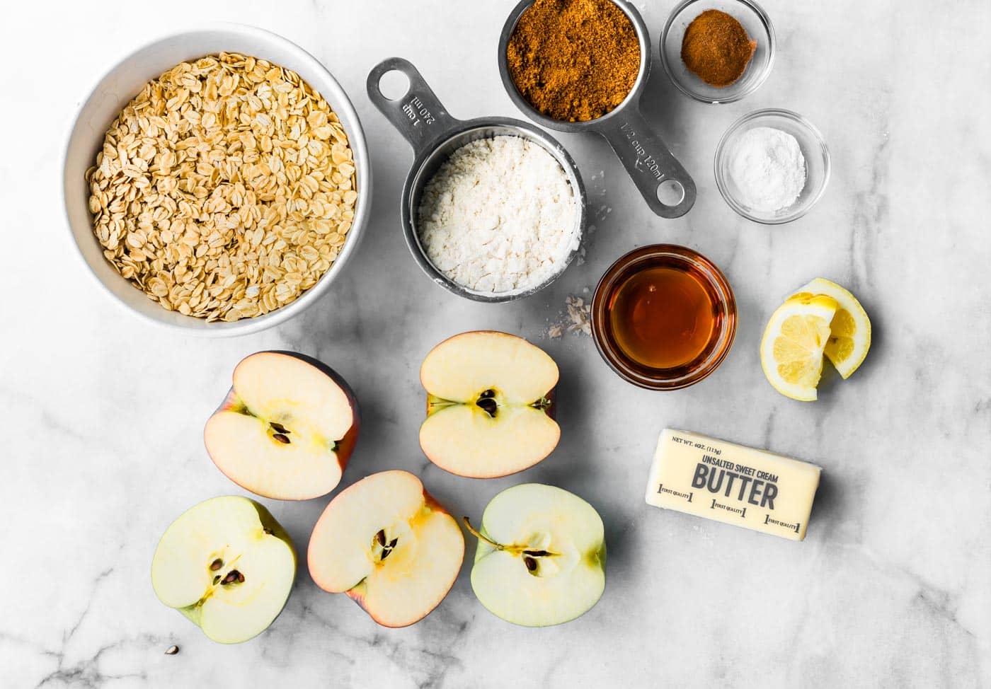 Fresh apples, oats, butter, maple, flour, sugar, lemon, and spices for apple crisp bars ingredients.