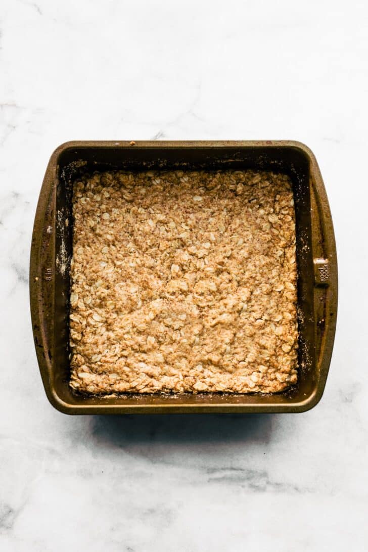 baked oat crust in square baking pan for gluten-free apple crisp bars.