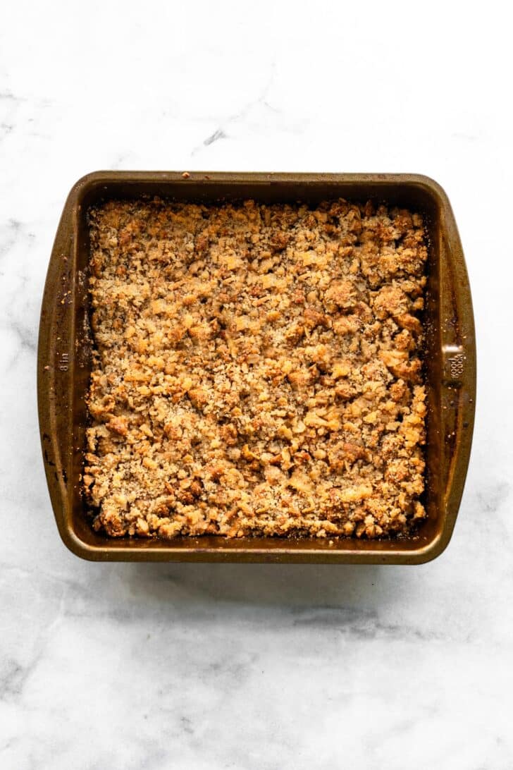 Baked apple crisp bars cooling in pan with golden brown oat crumble topping.