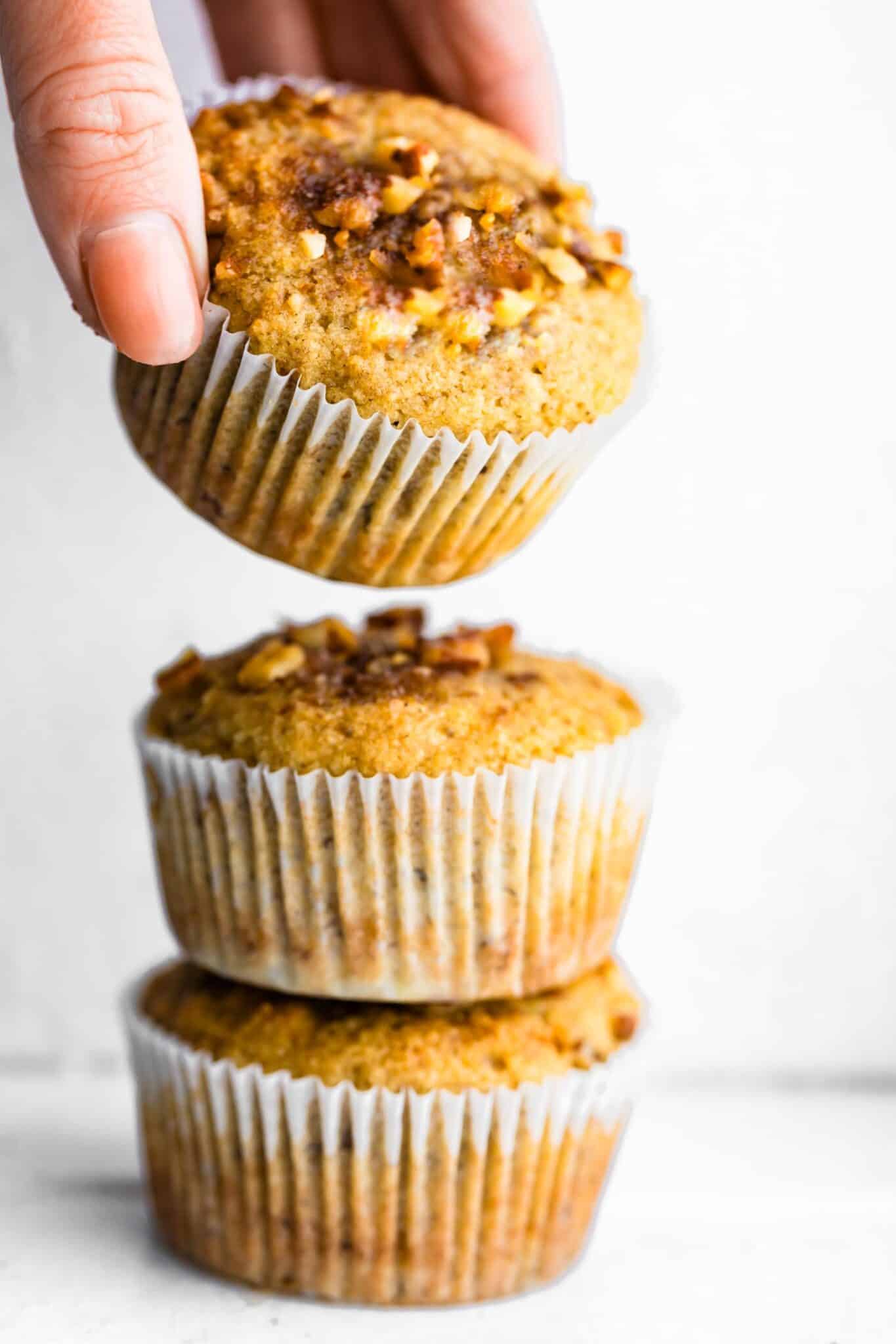 A woman's hand lifting the top muffin off of a stack of banana muffins.