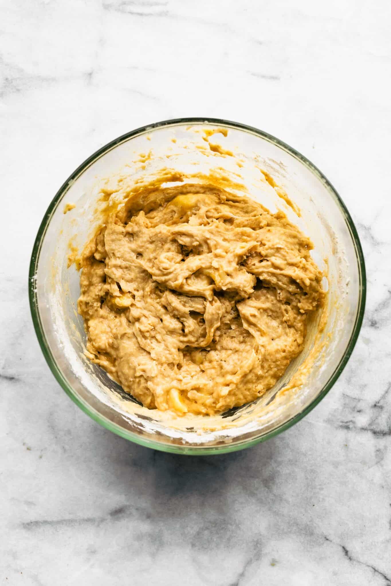 Banana muffin batter in a glass mixing bowl.