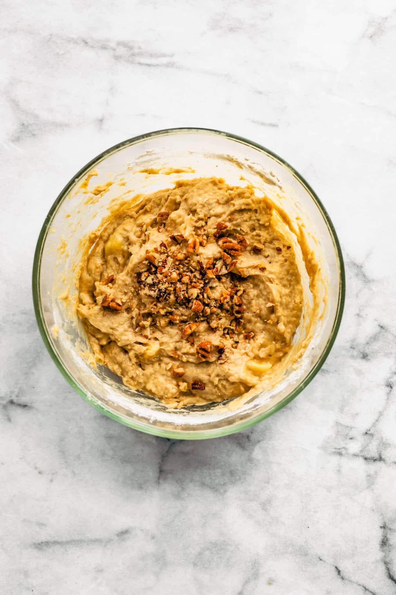 Banana muffin batter with nuts in a glass mixing bowl.