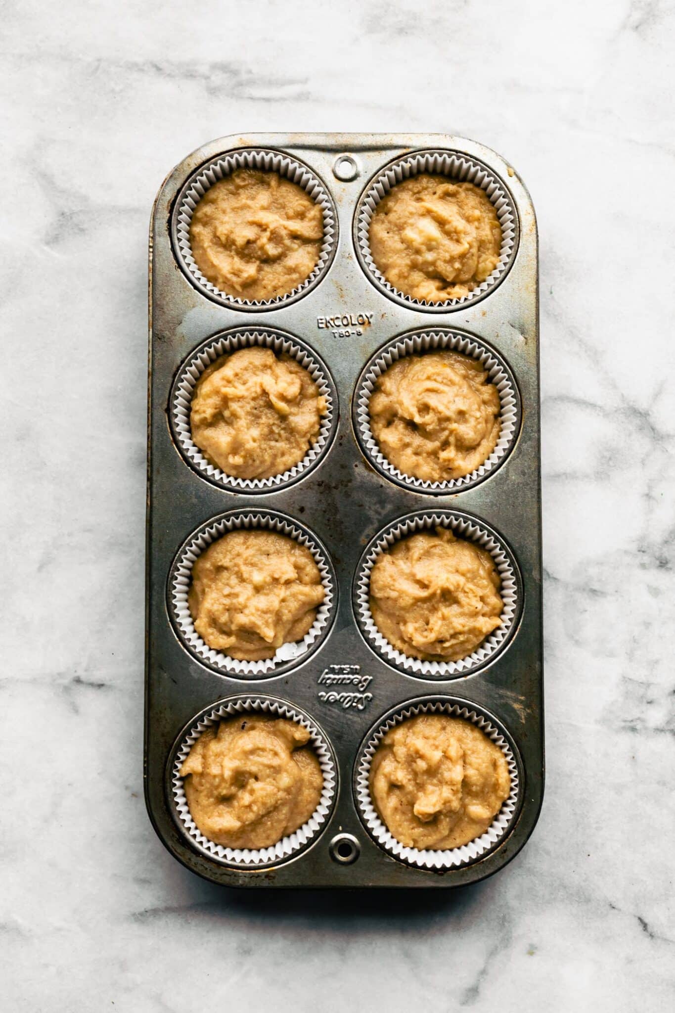 Eight count muffin pan with muffin liners filled with banana muffin batter.
