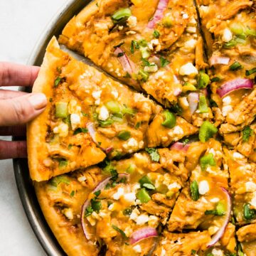 A woman taking a slice of a homemade BBQ chicken pizza.