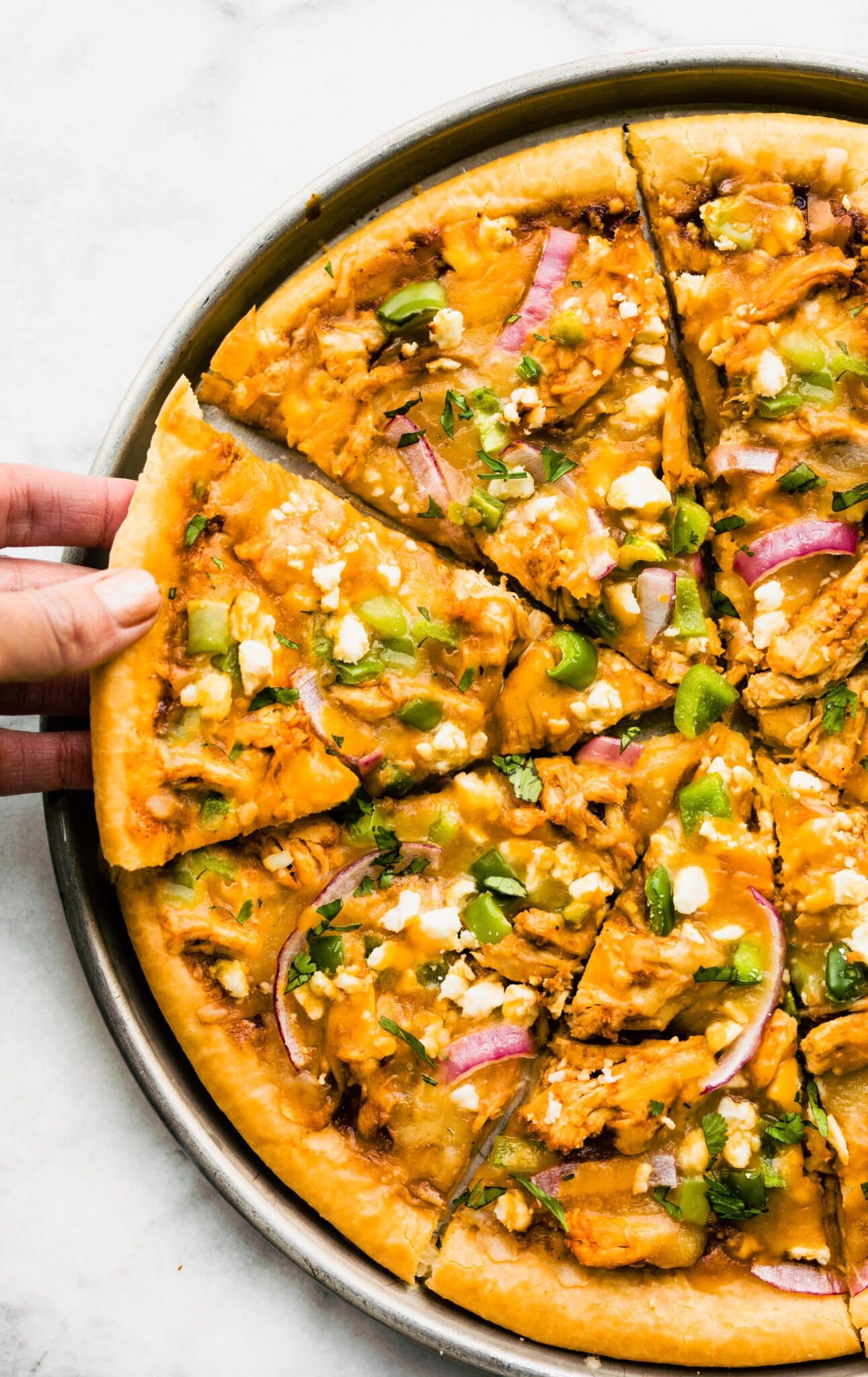 A woman taking a slice of a homemade BBQ chicken pizza.