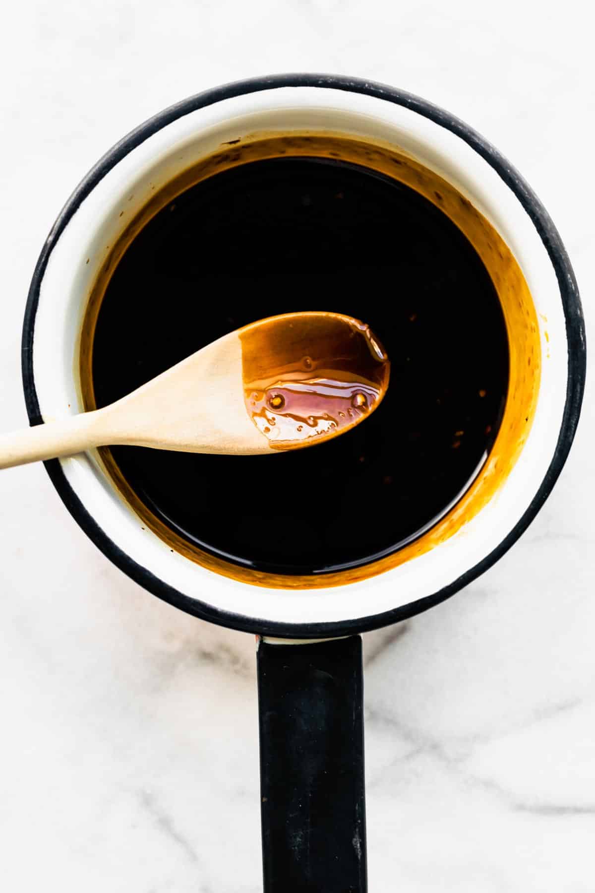Overhead photo of a wooden spoon with gluten free teriyaki sauce over a white pan.