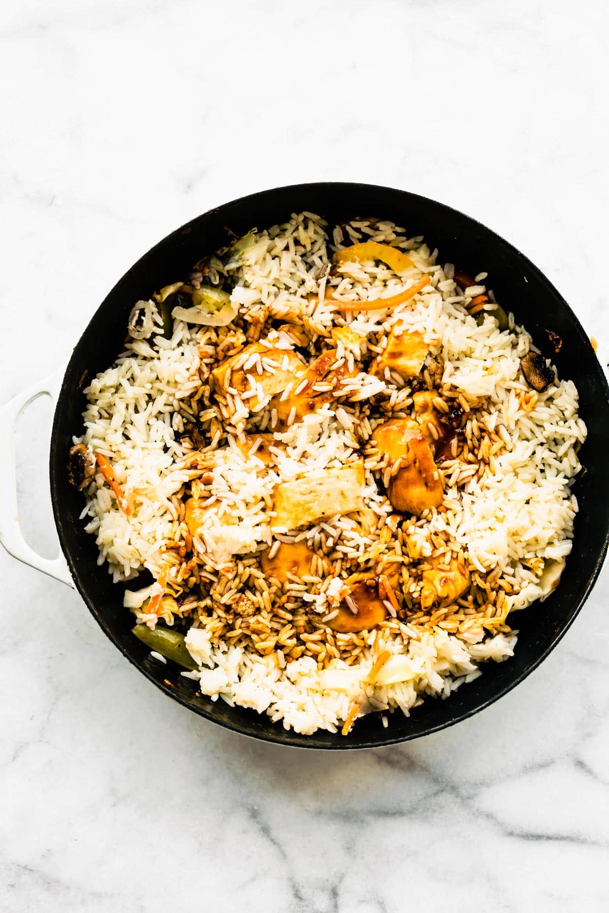 Cooked white rice and teriyaki sauce over cooked veggies and chicken in a black pan.
