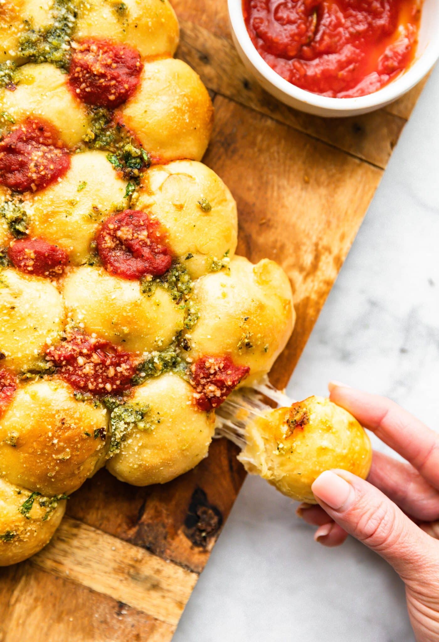 Up close photo of woman's fingers pulling a cheesy bread ball from a Christmas tree.