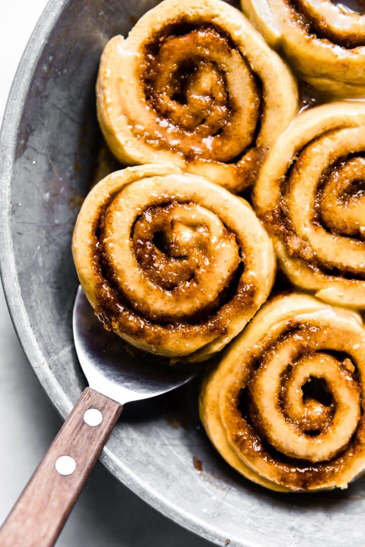 silver pan/plate with gooey gluten free cinnamon roll and serving spatula underneath