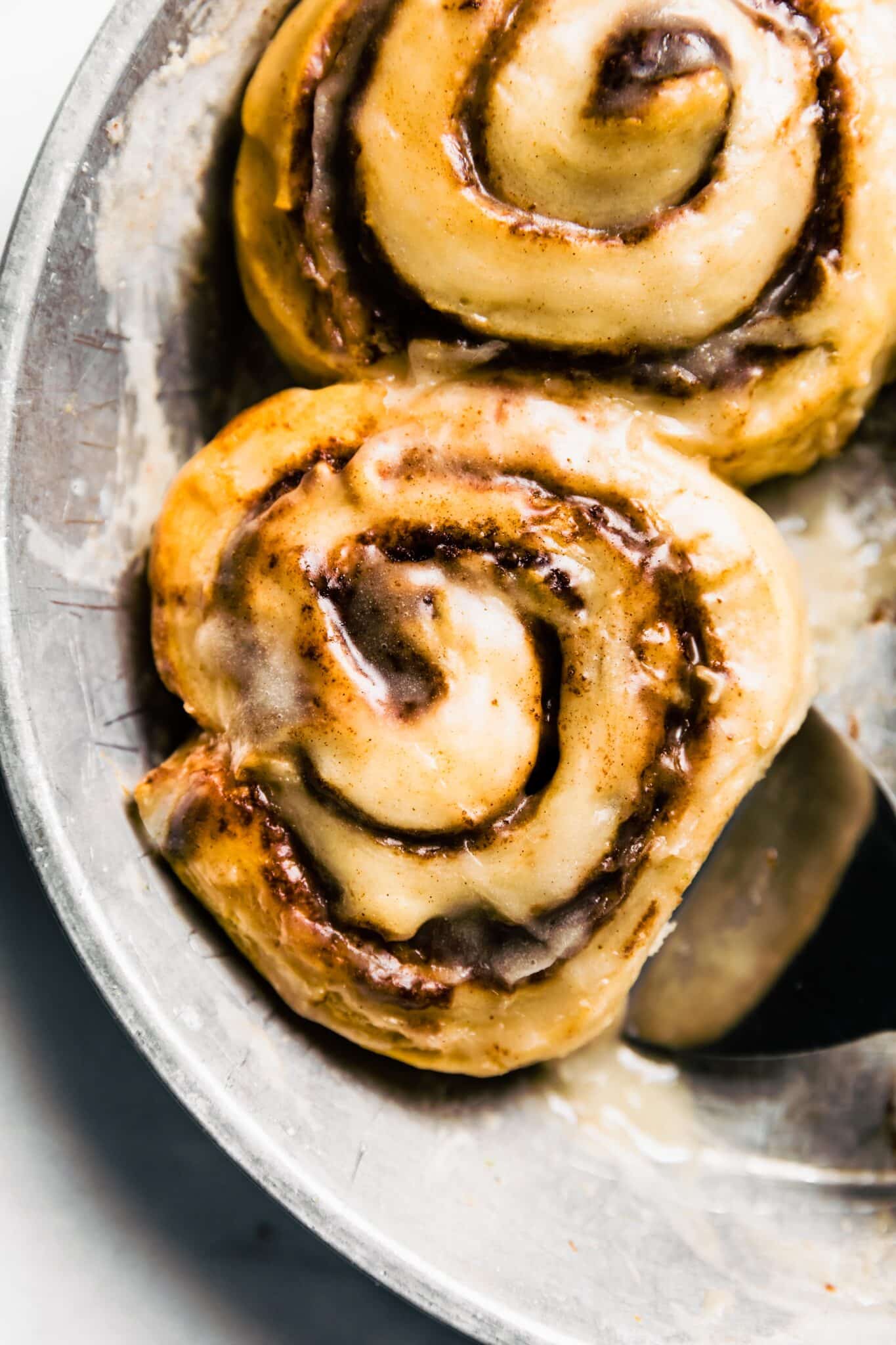 silver pan/plate with gooey gluten free cinnamon roll and serving spatula underneath