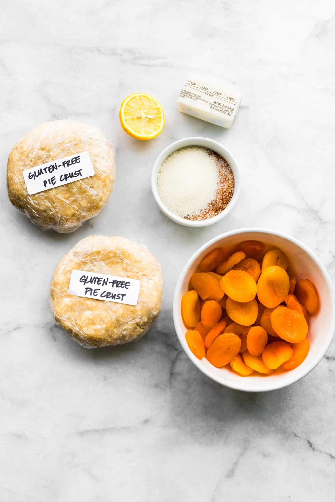 Ingredients for dried apricot pie laid out, including dried apricots, pie crust dough, sugar, butter, and a lemon