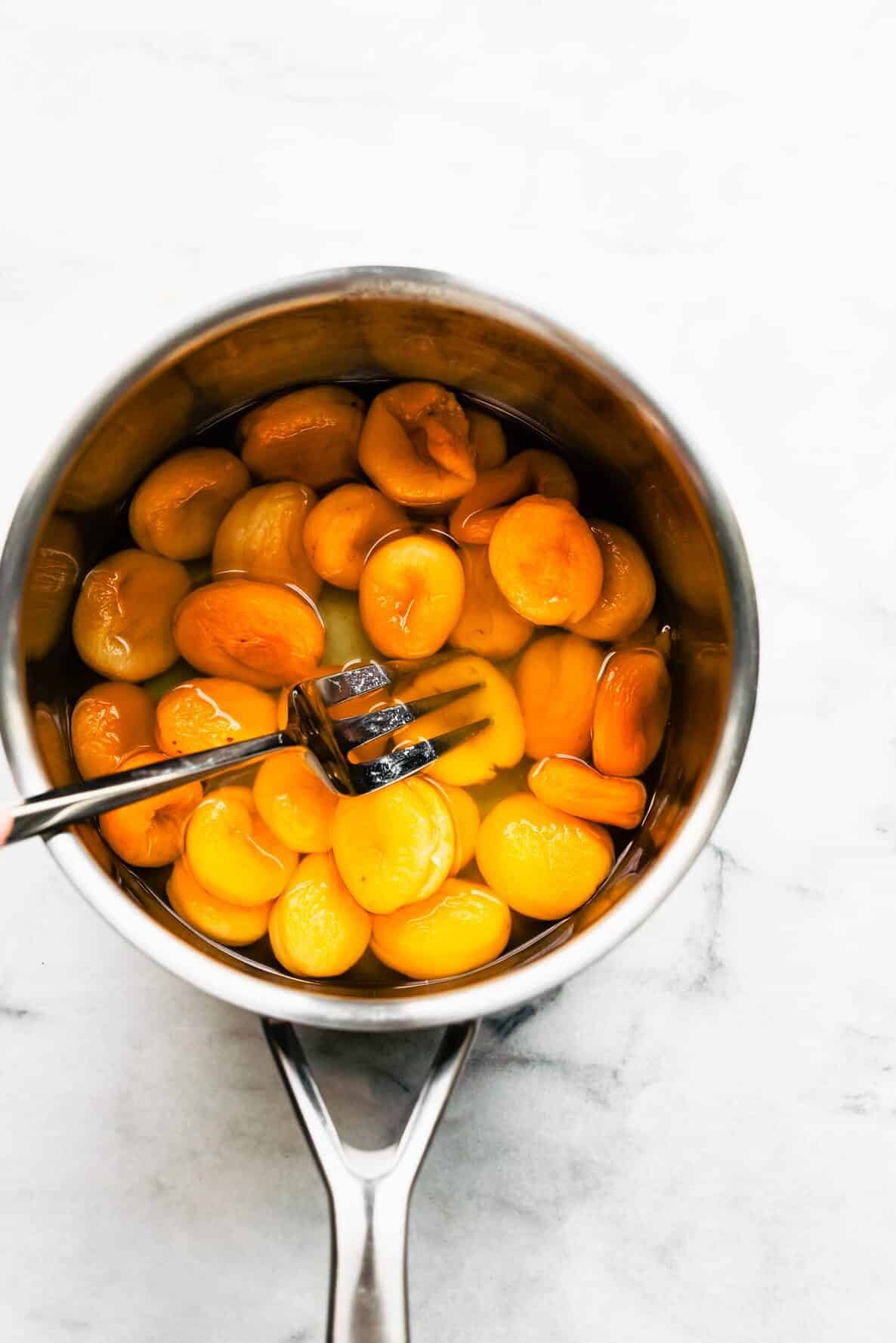 Woman's hand mashing dried apricots with a fork in a pot