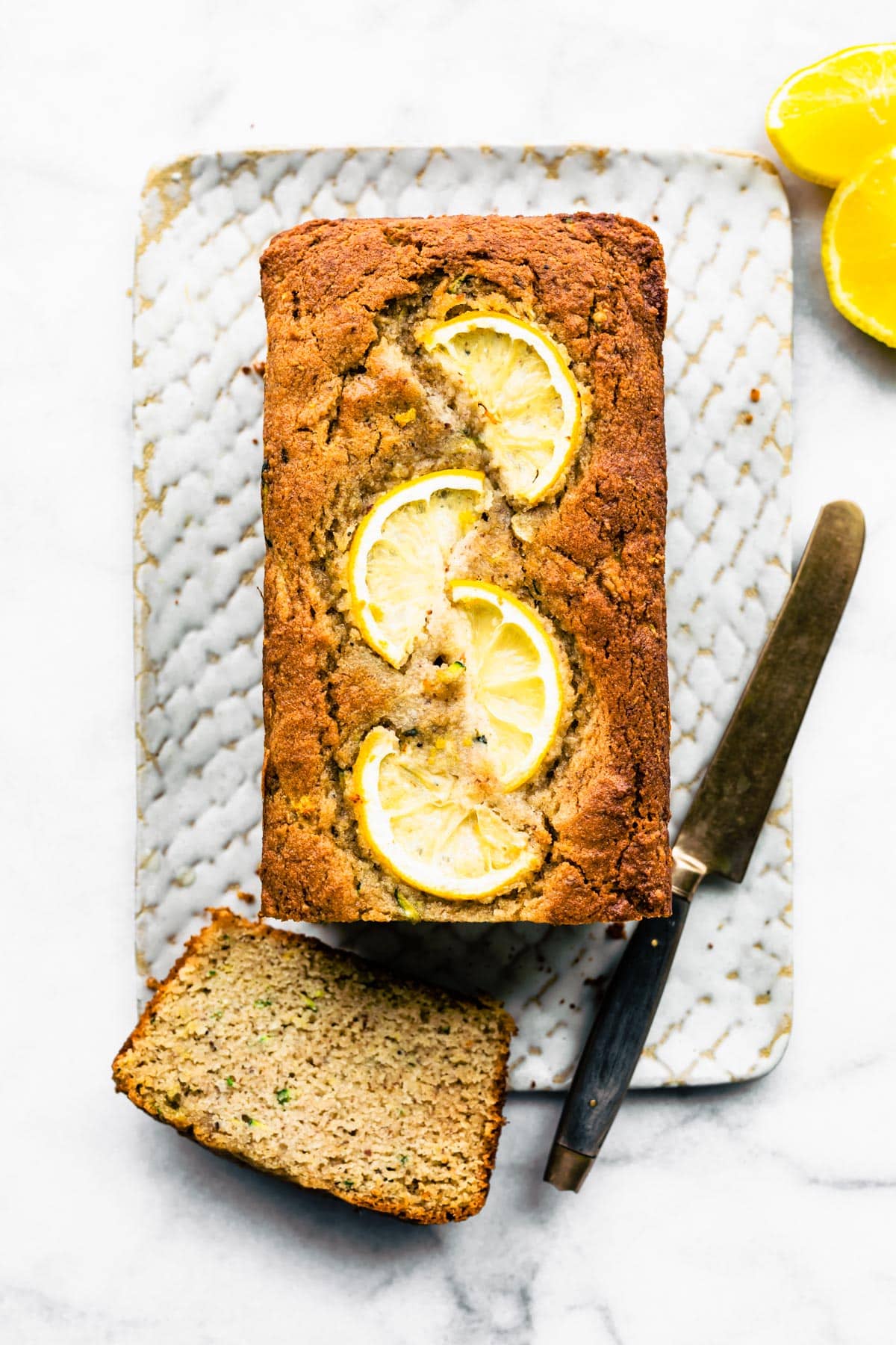 Overhead image of a loaf of lemon zucchini bread with a piece cut off.