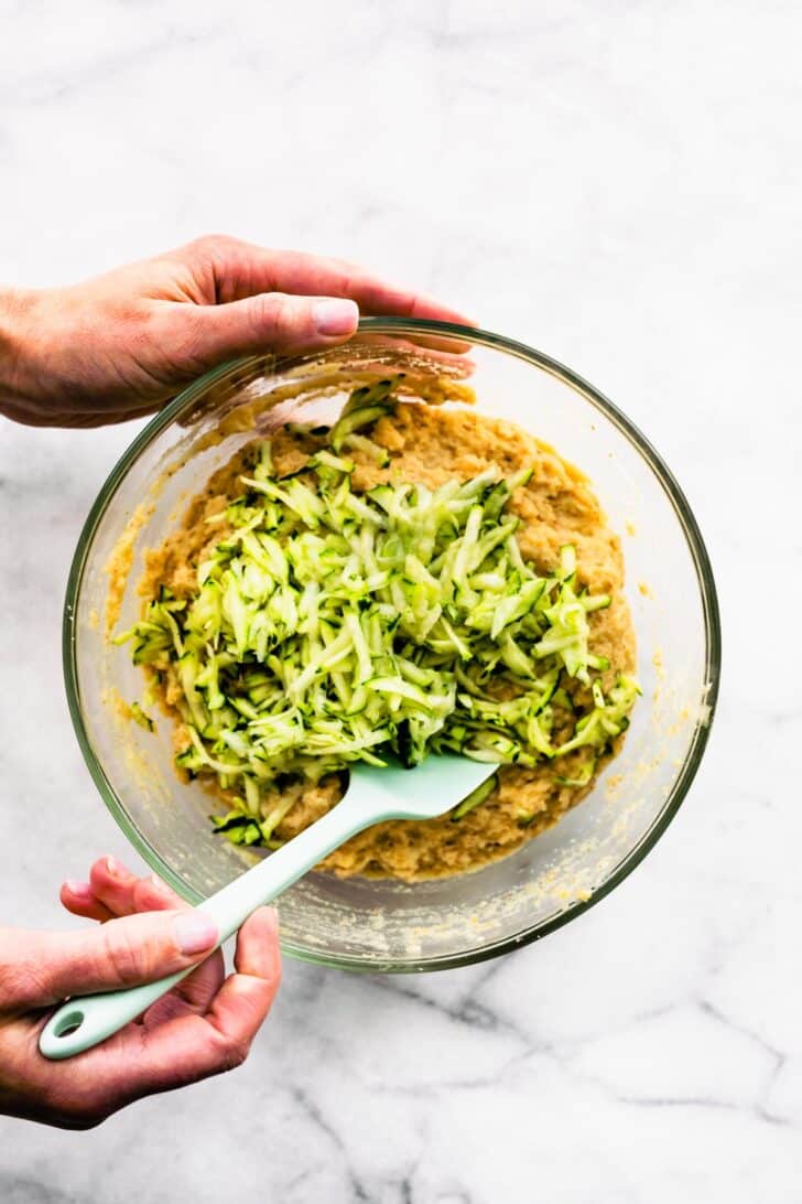 Two hands stirring the batter for lemon zucchini bread.