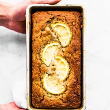 Two hands holding a baked loaf of lemon zucchini bread.
