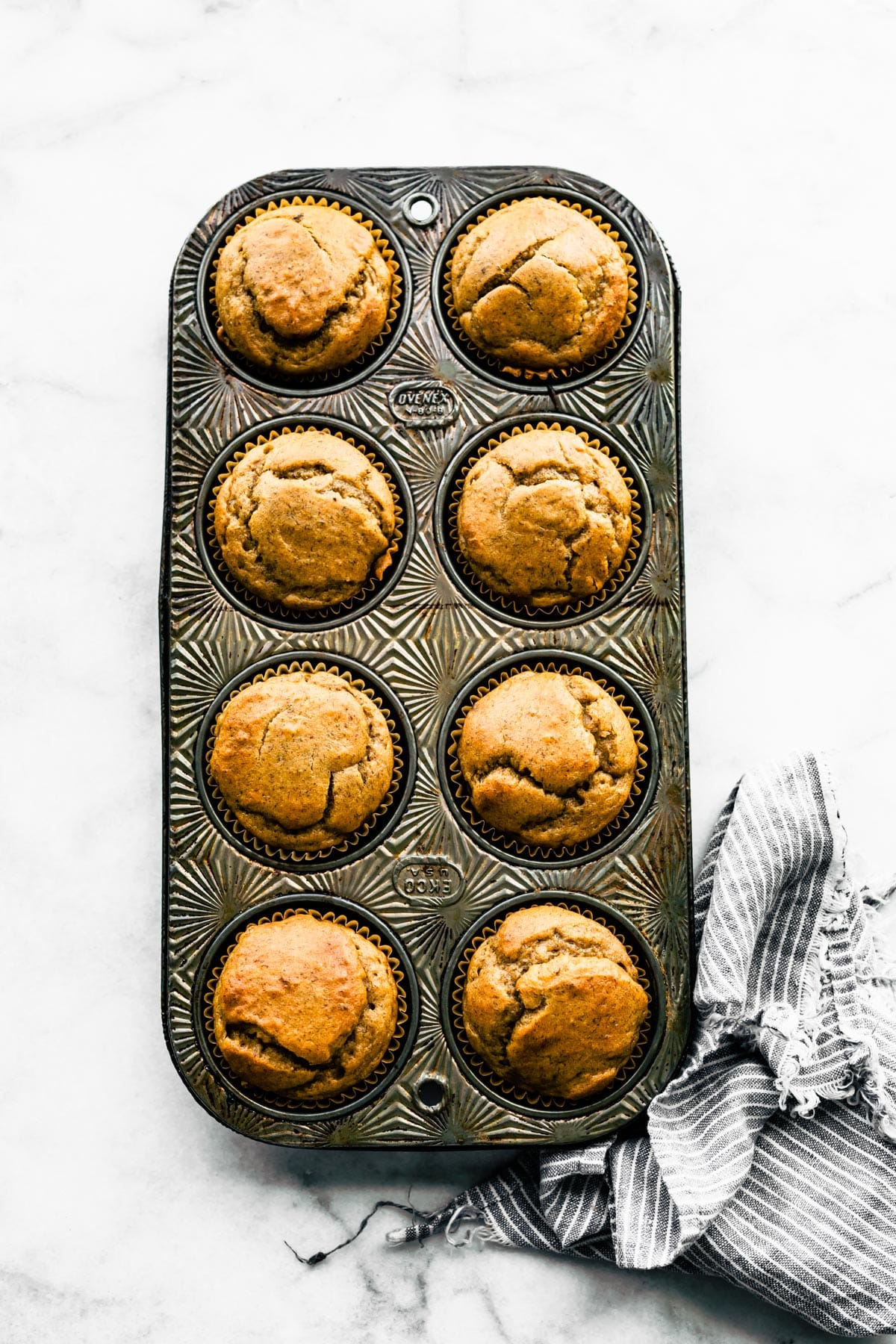 Eight baked healthy banana muffins in a vintage muffin tin.