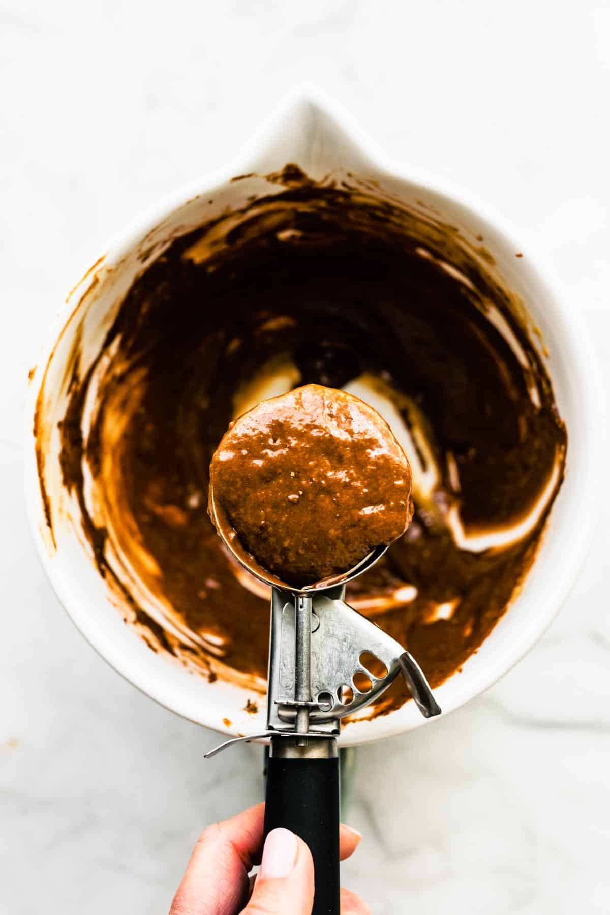 A cookie dough scoop with chocolate protein banana muffin batter.