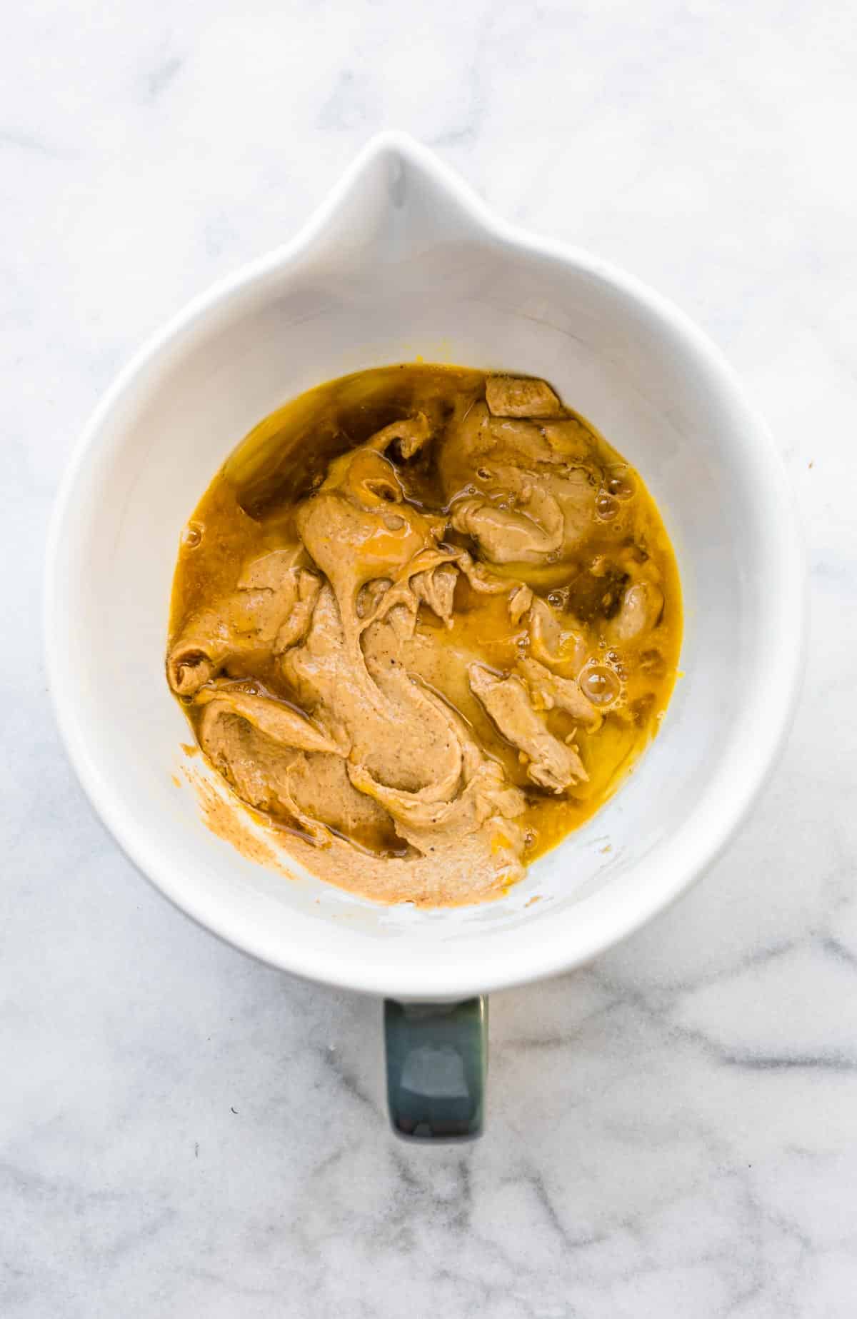 Peanut butter banana mixture in a white mixing bowl with maple syrup and eggs.
