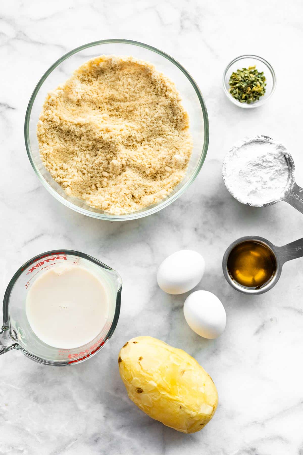 Almond flour, non dairy milk, and a peeled baked potato on a white marble countertop.