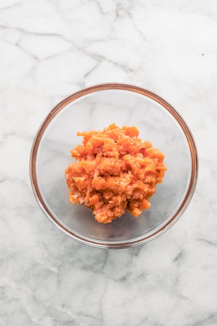 Fresh salmon cut into small chunks in a clear glass bowl.
