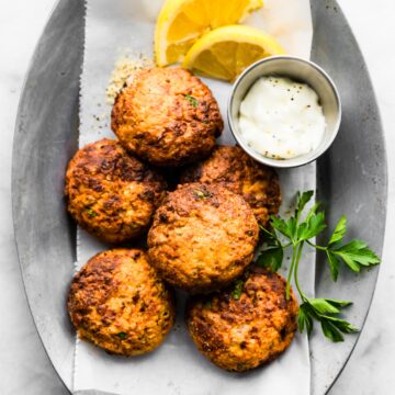 Plate of stacked tuna patties on a silver platter with dipping sauce and lemon/herbs.