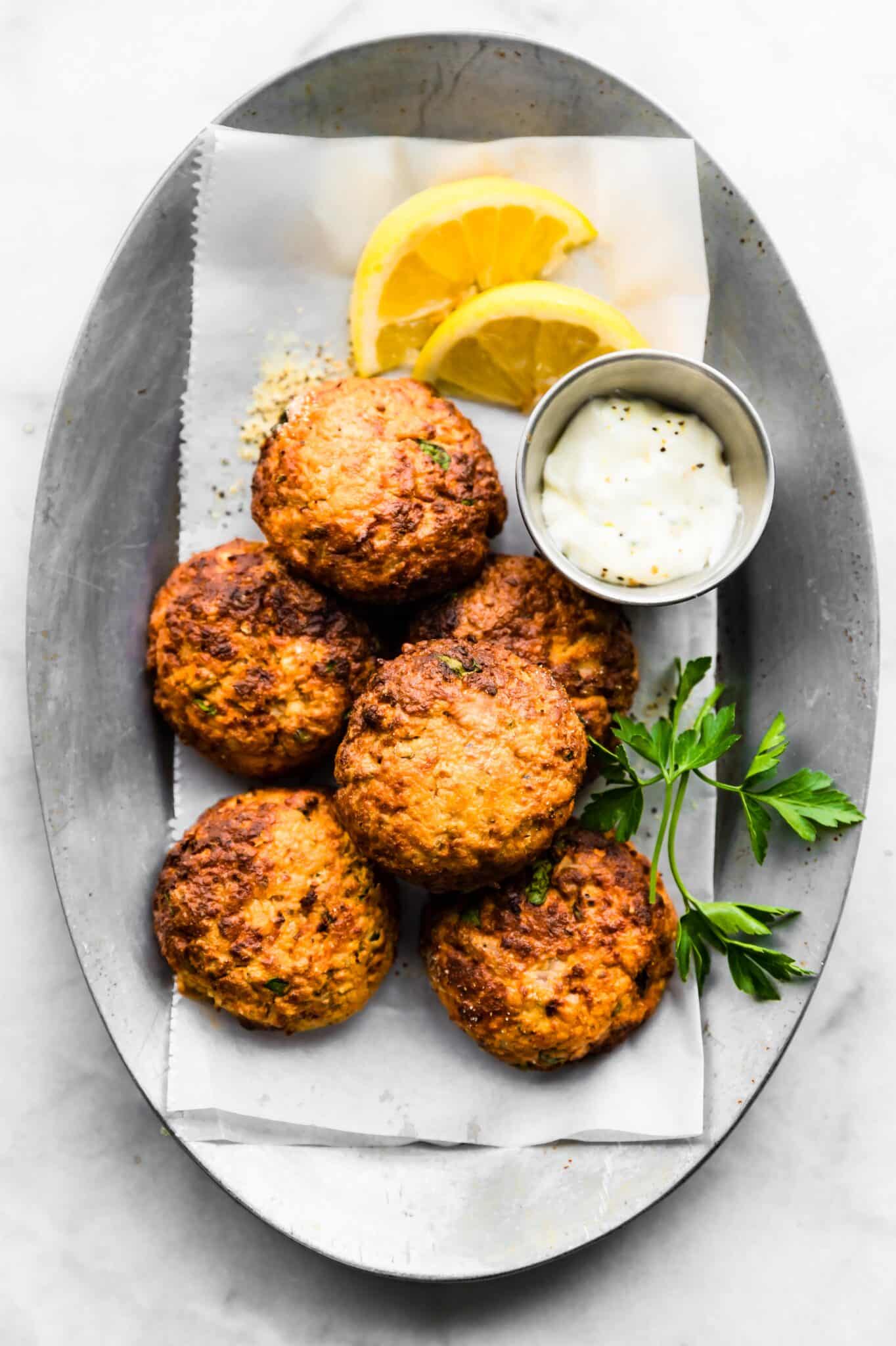 Plate of stacked tuna patties on a silver platter with dipping sauce and lemon/herbs.