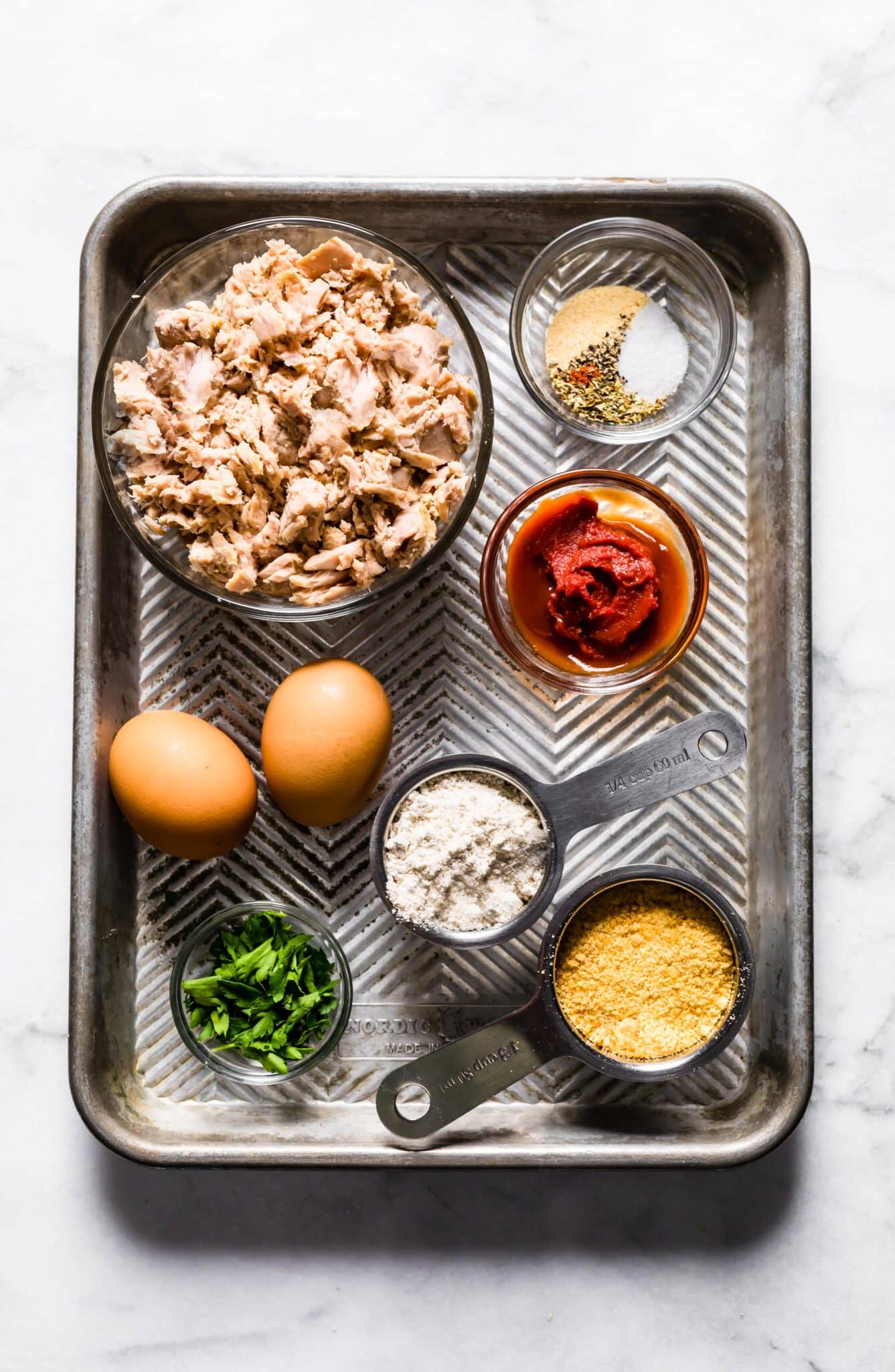 Gluten free tuna patty ingredients in bowls on a metal sheet pan.