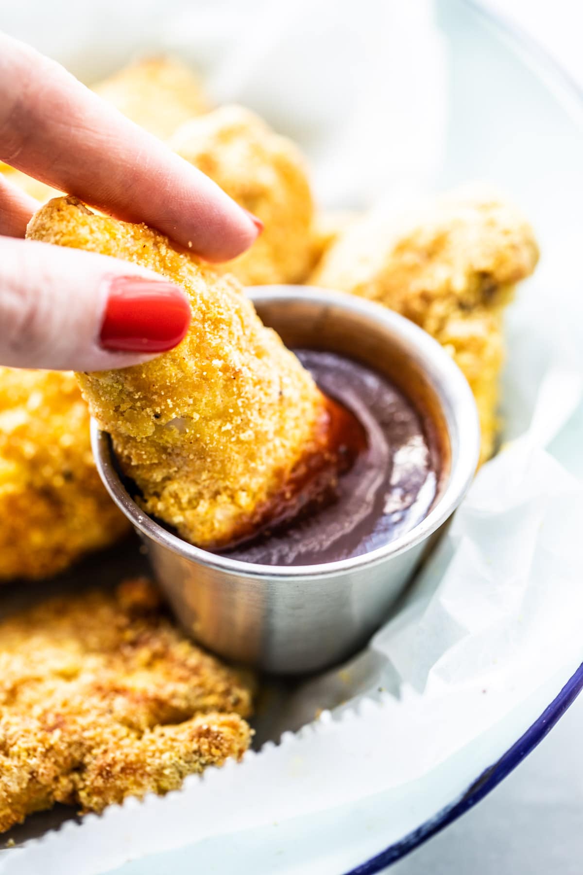 woman's fingers dipping chicken strip into bbq sauce