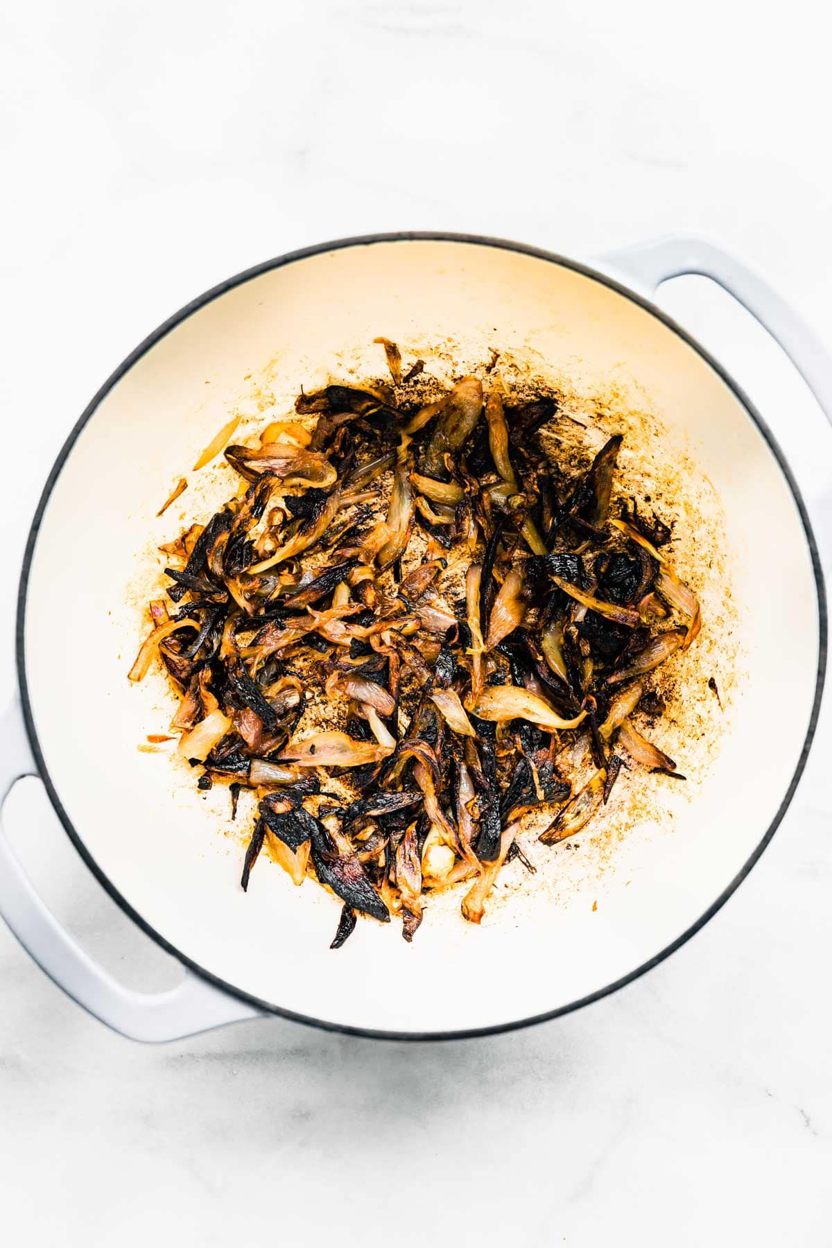 Overhead photo of crispy fried shallots in a white pan on a marble countertop.