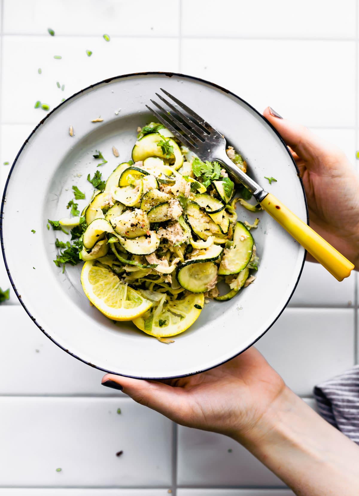 Paleo Tuna Green Chile Zoodle Casserole on white plate in woman's hands. Herbs on side