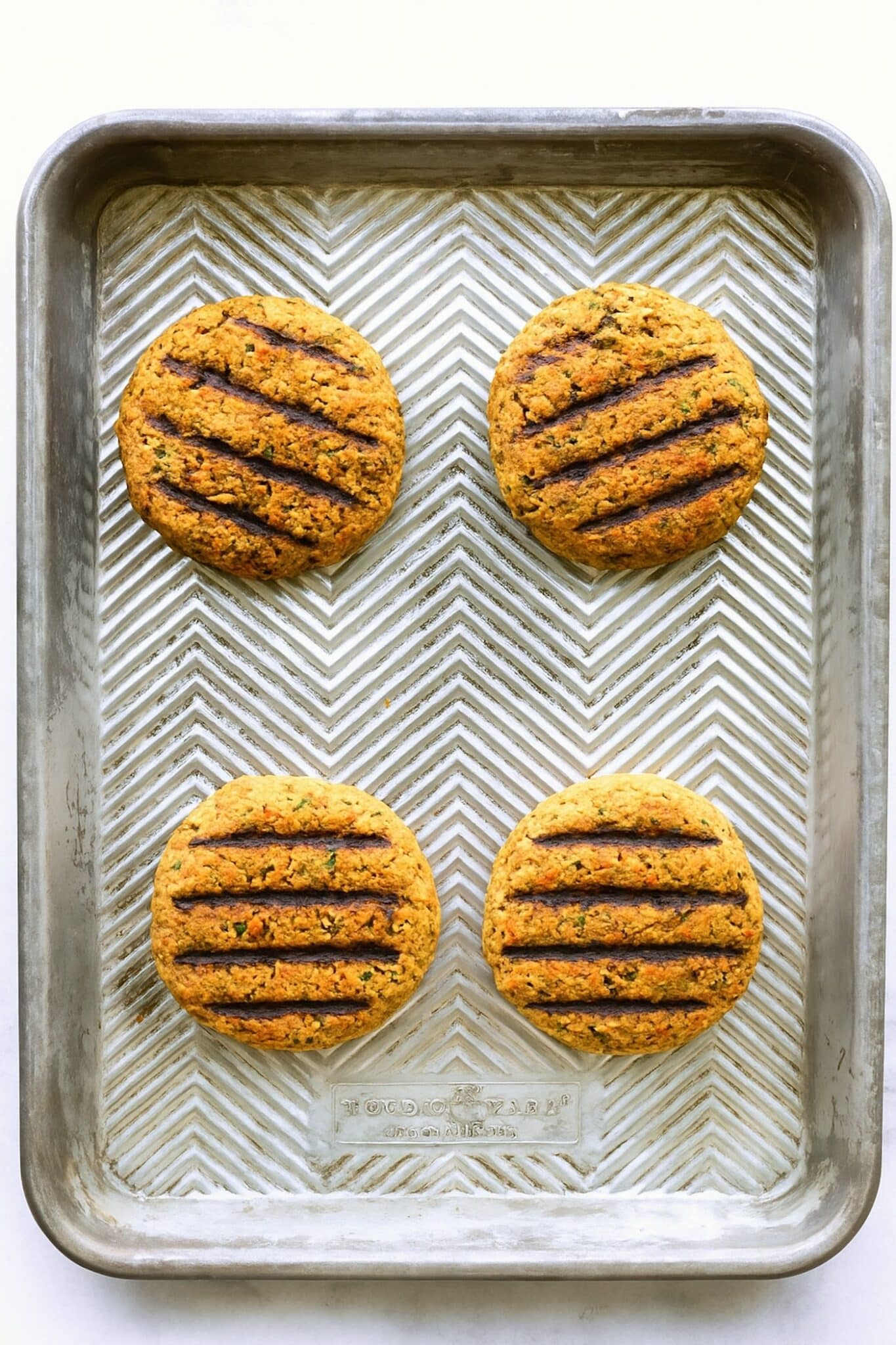Four grilled veggie burgers on a metal sheet pan.