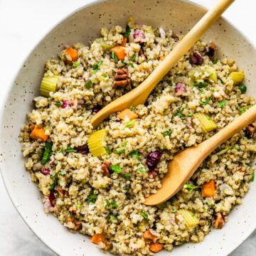 Two wooden serving spoons in a bowl of pretty quinoa with veggies.