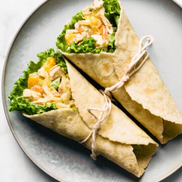 Photo of two Asian chicken salad wraps on a plate tied closed with a string.