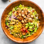 BBQ tempeh, corn, tomatoes, and red onion on chopped romaine in a wooden bowl.