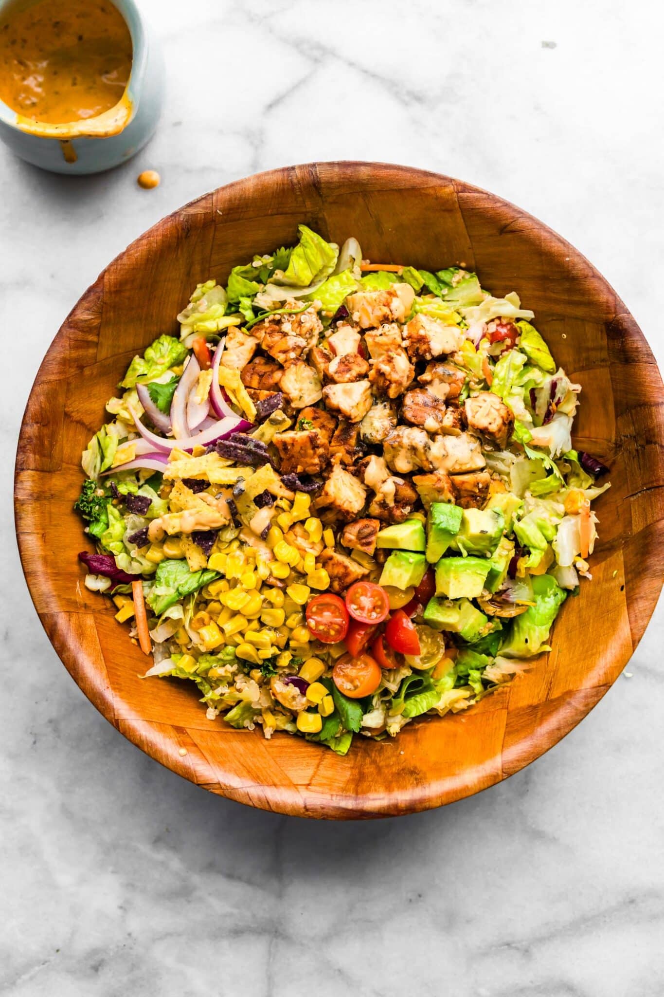 BBQ tempeh, corn, tomatoes, and red onion on chopped romaine in a wooden bowl.